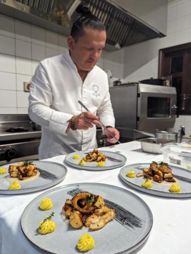 a chef standing in a kitchen with four plates of food at La Belle Tortue in Silhouette Island