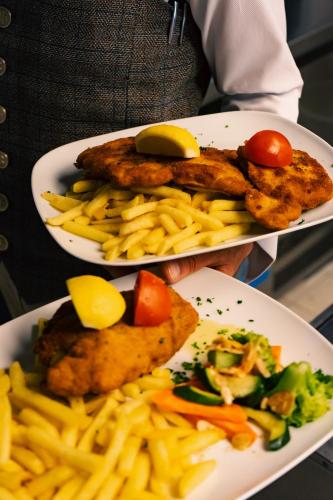 a person holding two plates of food with french fries at Ospizio La Veduta in Bivio