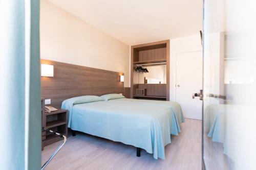 a bedroom with a bed with a blue blanket and a table at Apartamentos Loar in Ferreries