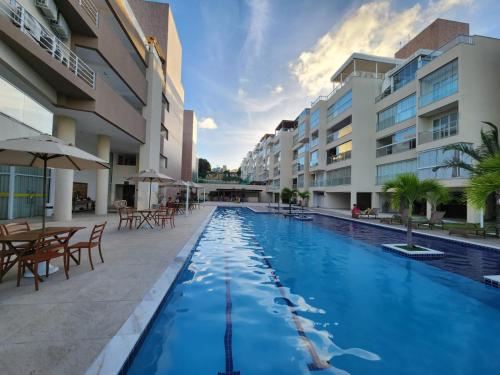 - une piscine avec des tables et des chaises à côté des bâtiments dans l'établissement APART Alto padrao praia PIRANGI, à Parnamirim