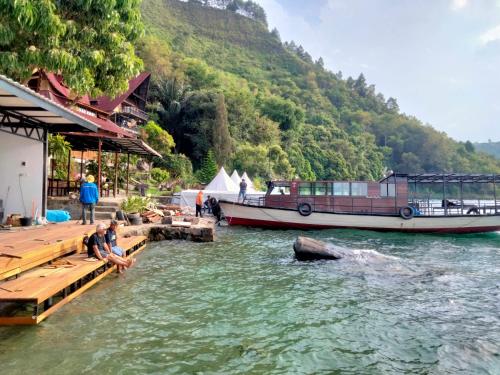 a man sitting on a dock next to a boat at Pondok Berata Dapdap in Balige