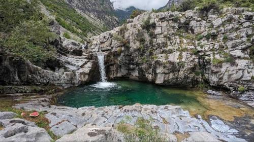 a pool of water in a canyon with a waterfall at Vilat Pllumaj in Gropat e Selcës