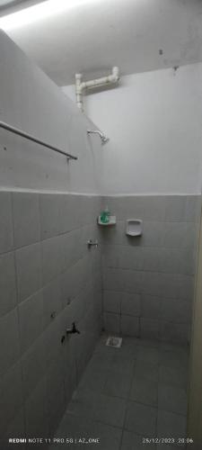 uma casa de banho com um chuveiro, piso em azulejo e azulejos brancos em MY HOMESTAY PANGSAPURI SUTERA 2 em Kampong Telok