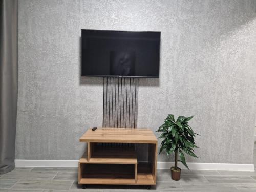 een tv aan een muur met een tafel en een plant bij Аренда in Temirtaū