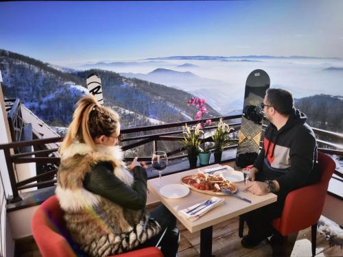 a man and woman sitting at a table with a plate of food at Apartmansko naselje DVORI in Kopaonik