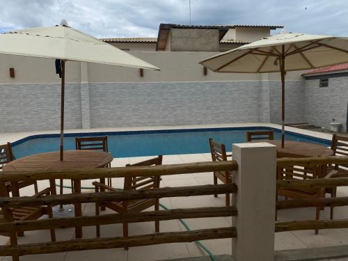 twee tafels en parasols naast een zwembad bij Pousada Casa da Praia SFI in Sao Francisco do Itabapoana