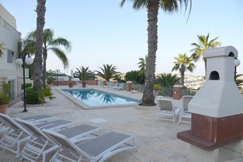 a pool with chaise lounge chairs and a resort with palm trees at Villa Lyss Apartment 1 in Mellieħa