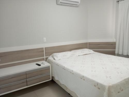 a white bedroom with a bed and a nightstand at Ótimo Apartamento vista mar a 70 metros in Itapema