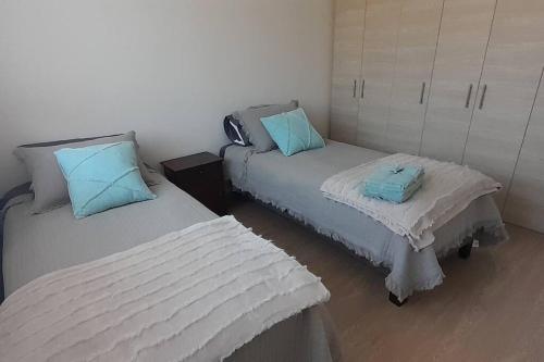 Duas camas num pequeno quarto com almofadas azuis em Dpto. nuevo una cuadra del lago. em Villarrica