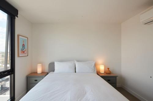 a bedroom with a white bed with two candles on tables at Urban Rendezvous - Where Productivity Meets Play in Melbourne