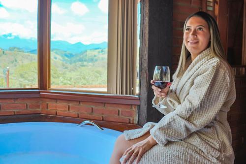 a woman sitting next to a tub holding a glass of wine at Chalé Encanto da Natureza in Visconde De Maua
