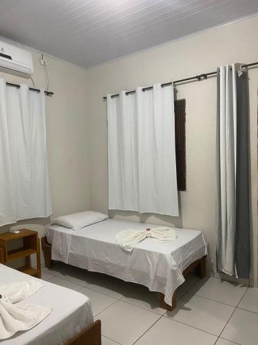 two beds in a room with white walls and curtains at Estrela dos Lençóis in Atins
