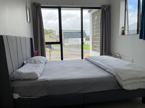 a bed in a bedroom with a large window at Totara Vale, Free Coffee, parking and wifi, near Glenfield Mall and highway 18,1 in Auckland