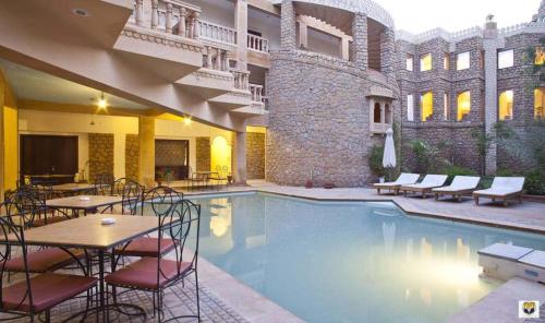 una piscina de hotel con mesas y sillas y un edificio en Hotel Deoki Niwas Palace, en Jaisalmer