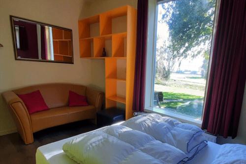 a bedroom with a bed and a window and a couch at De Opkikker 10 persoons vakantiehuis met hottub in Giethoorn