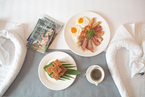 two plates of breakfast food with a book and a cup of coffee at White Corner Hotel in Phnom Penh