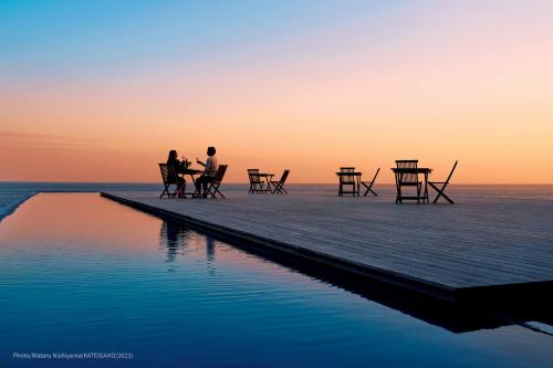 dos personas sentadas en una mesa en un muelle sobre el agua en TheMana Village, en Tosashimizu