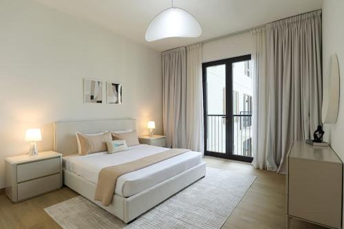 a white bedroom with a bed and a large window at HiGuests - Dream stay in our Cozy 2BR in La Rive Community in Dubai