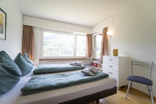 a bedroom with two beds with a window and a chair at Brentschpark 28 in Scuol