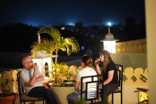 tres personas sentadas en una mesa en un balcón por la noche en Rajputana Heritage Ranthambhore Home Stay, en Sawāi Mādhopur