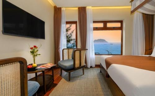 um quarto de hotel com uma cama e uma cadeira e uma janela em HA Hotel Apartments Ocean Front em Hoi An