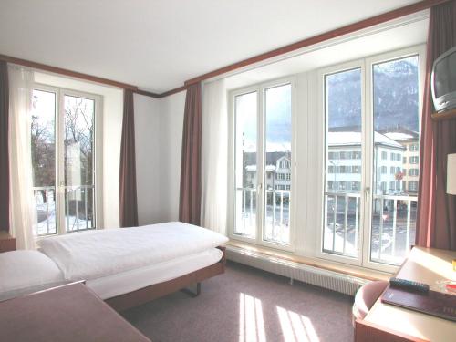 a bedroom with a bed and large windows at Hotel Post Glarnerhof in Glarus