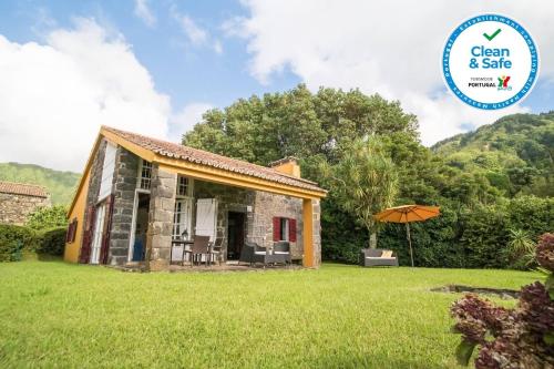 a small stone cottage with an umbrella in a yard at Casa da Lagoa in Sete Cidades