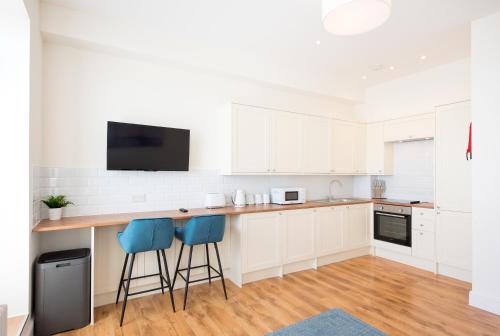 a kitchen with white cabinets and blue bar stools at Space Apartments - One Bed Seafront Apartment 4 in Harwich