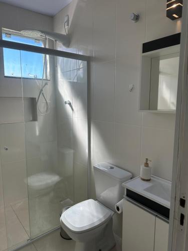 y baño blanco con aseo y ducha. en Residencial Valentina Jurere, en Florianópolis