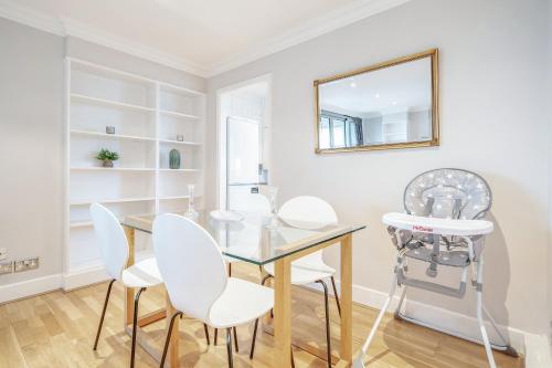 une salle à manger avec une table en verre et des chaises blanches dans l'établissement Stunning Flat on King's Road, Chelsea with Balcony, à Londres