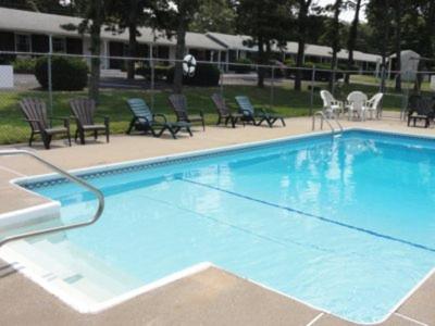 une grande piscine bleue avec des chaises et des tables dans l'établissement The Chatham Motel, à Chatham