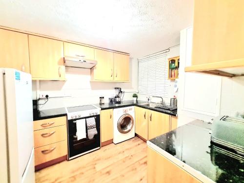a kitchen with wooden cabinets and a washer and dryer at Cosy Luxurious 3 Bedroom House, Free Parking, Free WiFi, Private Garden, Free Netflix in Havering atte Bower