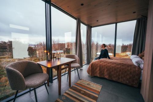 une femme assise sur un lit dans une pièce dotée de grandes fenêtres dans l'établissement WonderInn Arctic, à Utstrand