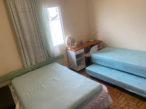 two beds in a room with a desk and a window at Apartamento Peruíbe com vista para o mar in Peruíbe