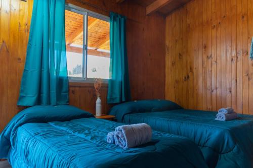 two beds in a room with blue curtains and a window at Mi Sueño Bed and Breakfast in Aluminé