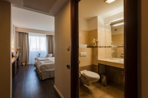 a bathroom with a toilet and a sink and a bed at Hotel Timisoara in Timişoara