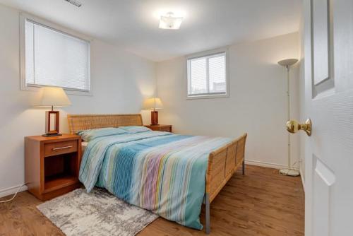 a bedroom with a bed and a nightstand and two windows at Comfortable Whitby 2 Bedroom Lower Suite in Whitby