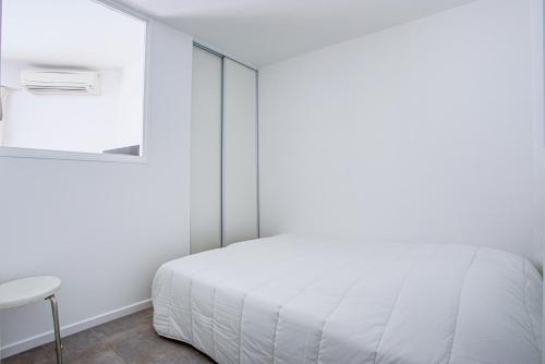 um quarto com uma cama branca e uma cadeira em Appartement T2 moderne avec terrasse clim parking et wifi - 4ALB3 em Perpignan