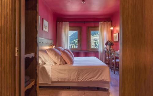 a bedroom with a bed with pink walls and a window at Hotel Aran La Abuela in Vielha