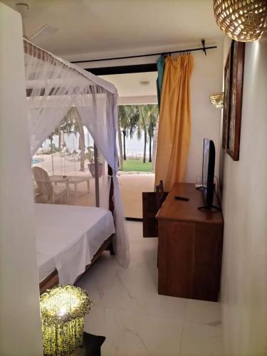 a bedroom with a bed and a desk and a television at Les Hibiscus sur Mer in Kabrousse