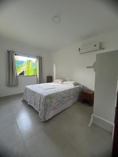 a white bedroom with a bed and a window at Residência Vittoria - Apartamento aconchegante em condomínio no centro de Arraial d Ajuda in Porto Seguro