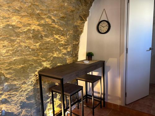 una mesa con dos taburetes y un reloj en una pared en Casa Cueva Sol y Luna Setenil en Setenil