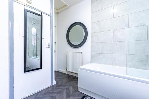 a white bathroom with a tub and a mirror at STAYZED R - Urban Oasis NG7, Walking Distance From City Centre & Lots of Amenities - Large bedrooms, Perfect for Work, Tourism, Family and Contractors - Long Stays Welcome in Nottingham