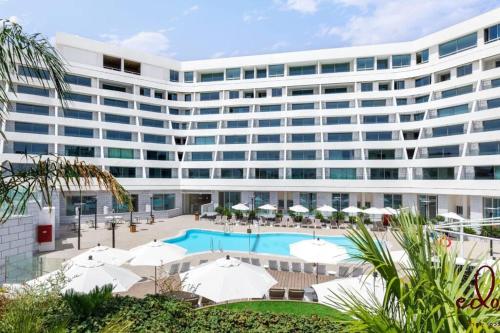 a large white building with a pool and umbrellas at דירה עם מרפסת על יד הים - By Edomlux in Eilat