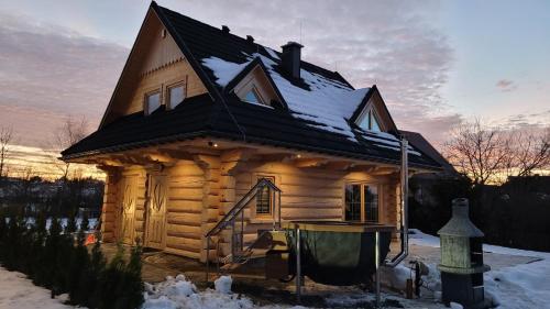 une cabane en rondins avec un toit noir dans la neige dans l'établissement Górskie Przysiółki w Koniakowie - Dom z bala KORONKA, à Koniaków