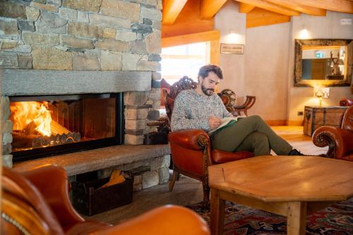 a man sitting in a chair in front of a fireplace at Au Charmant Petit Lac - Ecohotel Parc & Spa in Champoluc