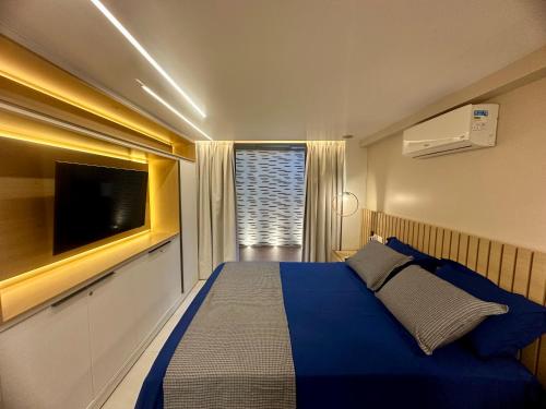 een slaapkamer met een blauw bed en een flatscreen-tv bij Flat Luxo - Pé na Areia - Maui Beach Residence in Tamandaré