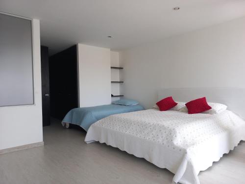 Dormitorio blanco con cama blanca y almohadas rojas en Lujoso Hospedaje en las Alturas, en Tunja