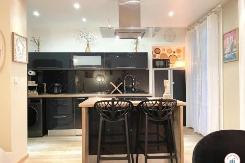 une cuisine avec des placards noirs et un comptoir avec des tabourets de bar dans l'établissement Bienvenue au Chillou - Parking - Terrasse, au Havre