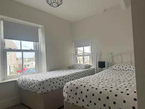 two beds in a white bedroom with two windows at Stable Door Cottage in Newquay